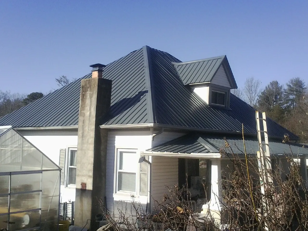 Dark blue standing seam metal roof on a white farmhouse with dormer — Slate & Tile Roof Repair by Roofing Brothers in Ghent