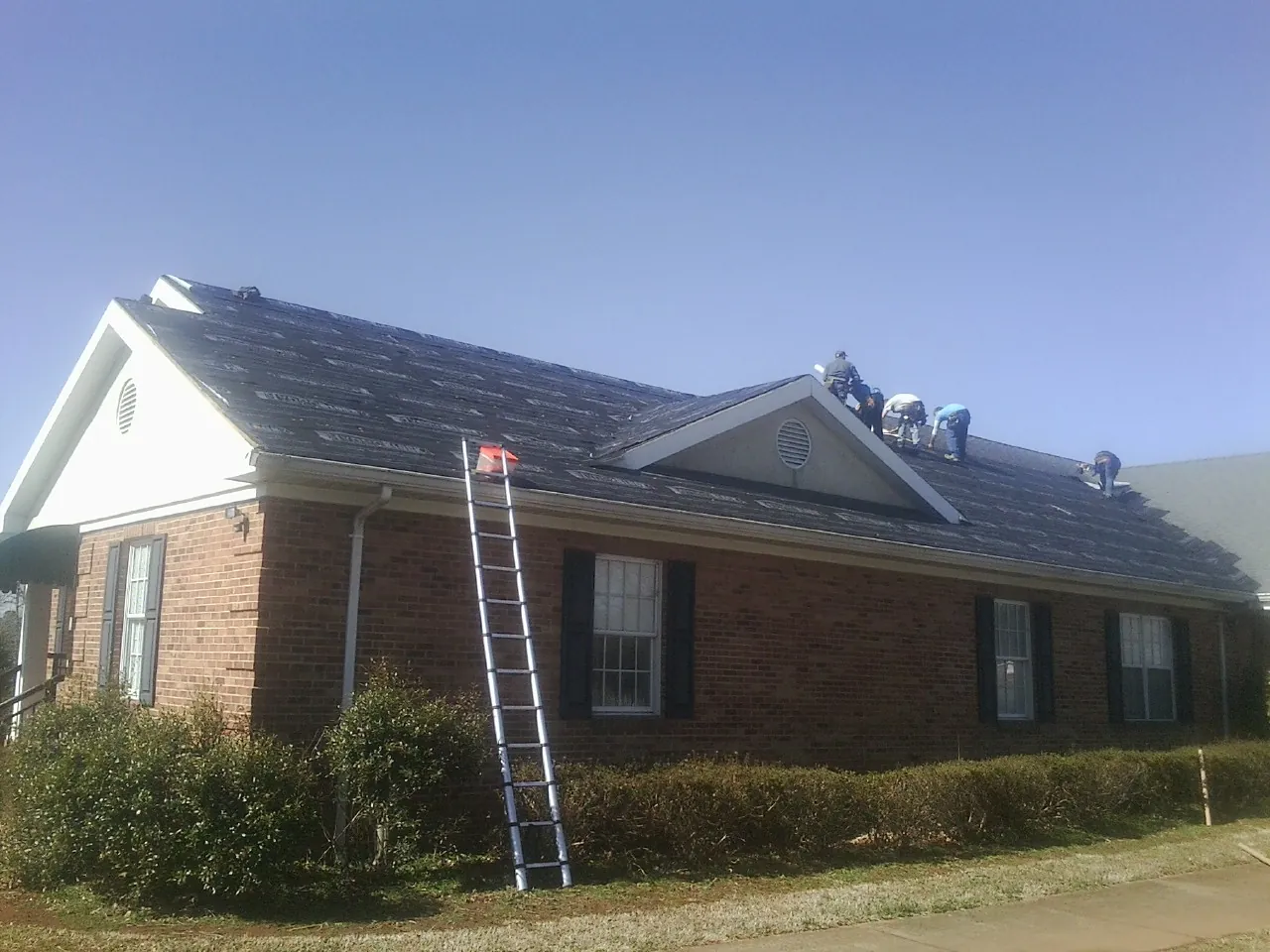 Crew tearing shingles off a brick ranch roof with a ladder set — Metal Roof Repair work by our crew in Ghent