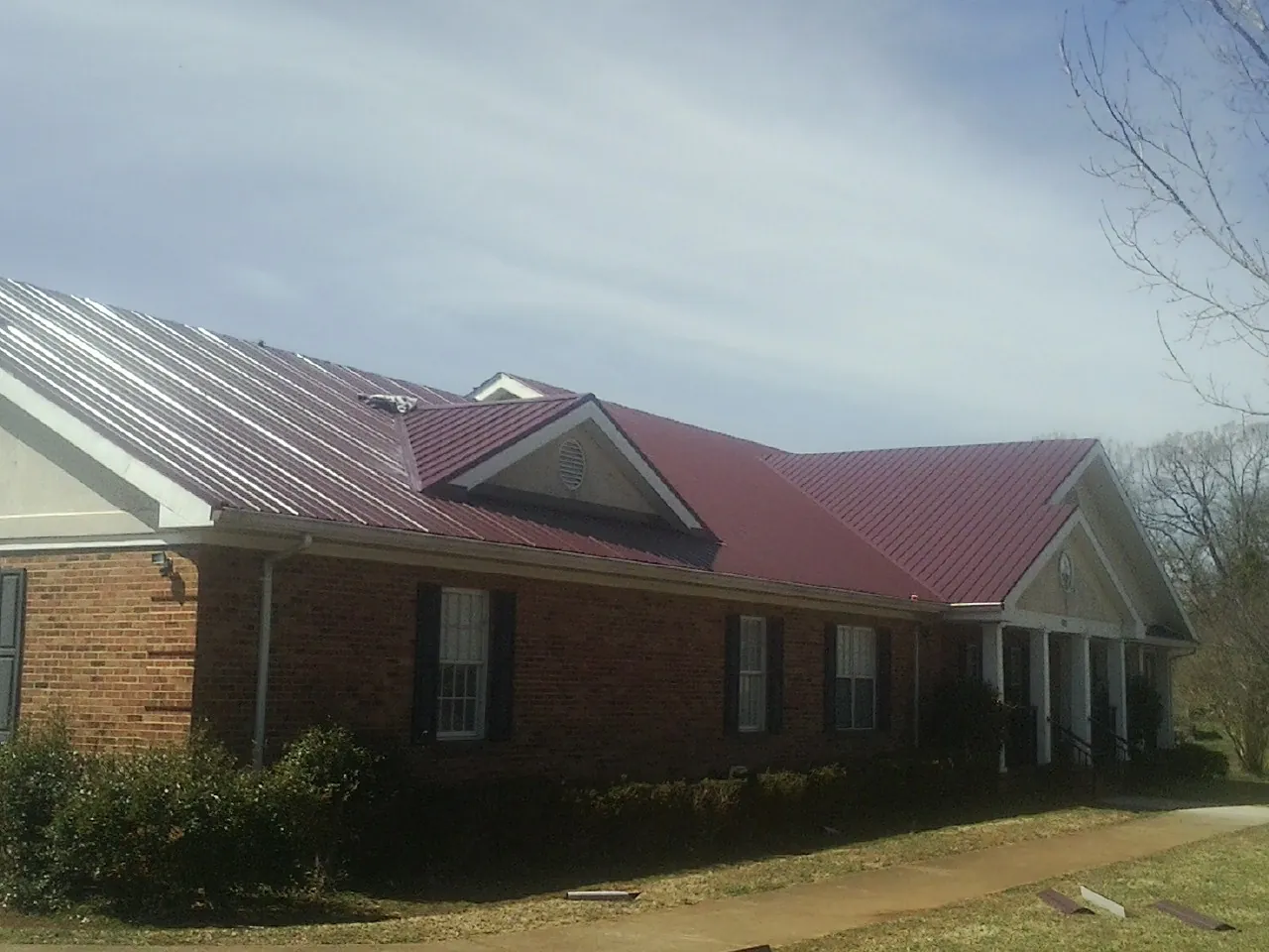 Red metal roof with gabled entries on a long brick building, from a Hail Damage Roof Repair job in Ghent