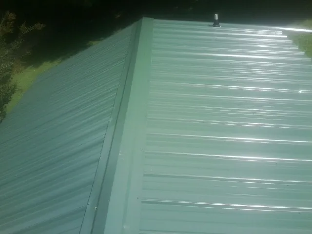 New green metal panels meeting at the ridge of a roof — Flat Roof Repair work by our crew in Ghent