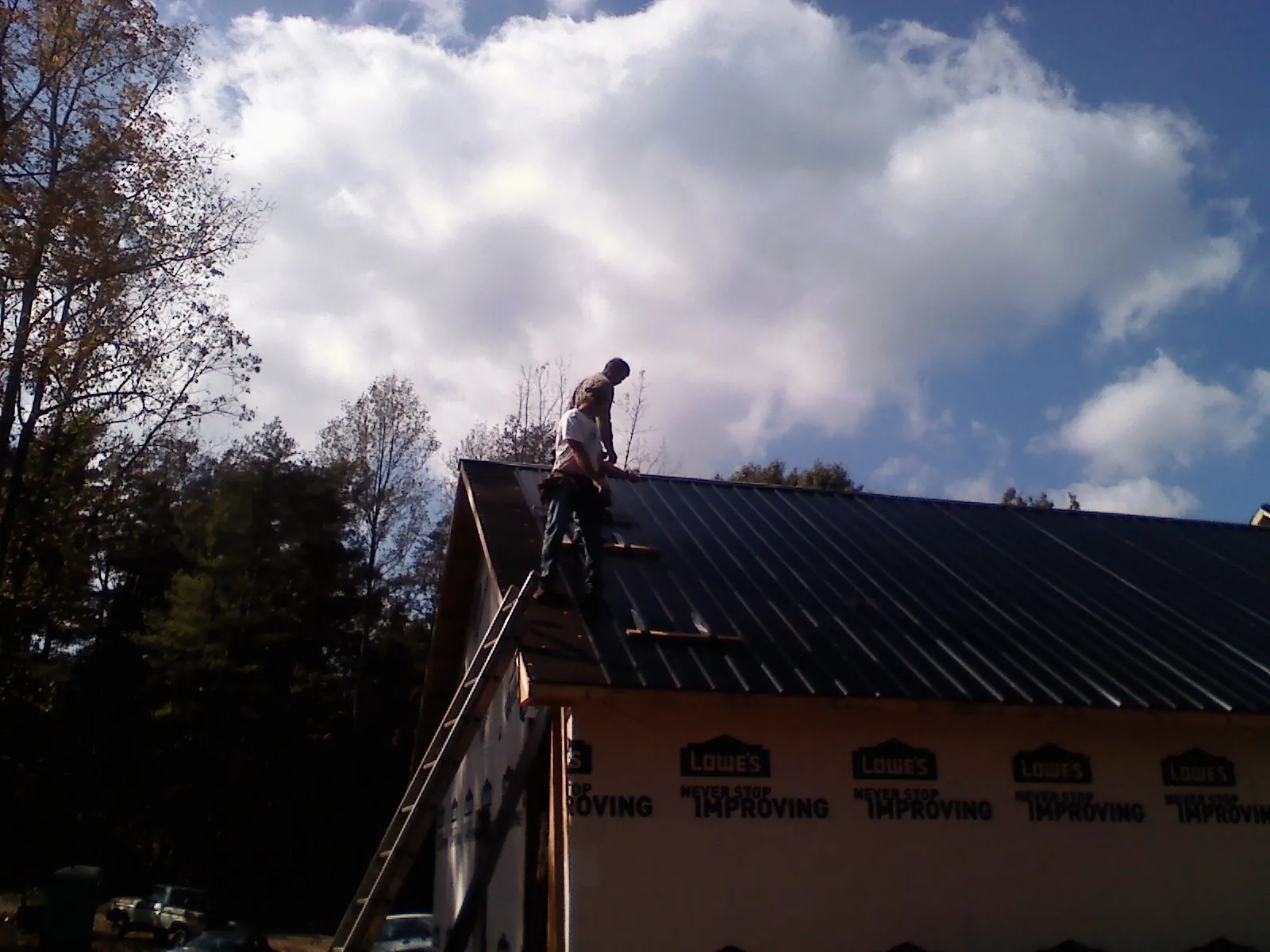 Roofer fastening dark metal panels high against a cloudy sky, from a Roof Inspection job in Ghent