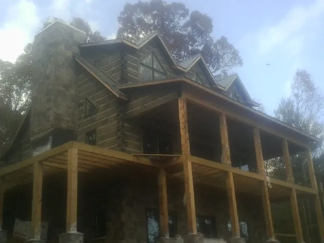 Stone chimney and dormers on a large log home with a timber porch in Ghent