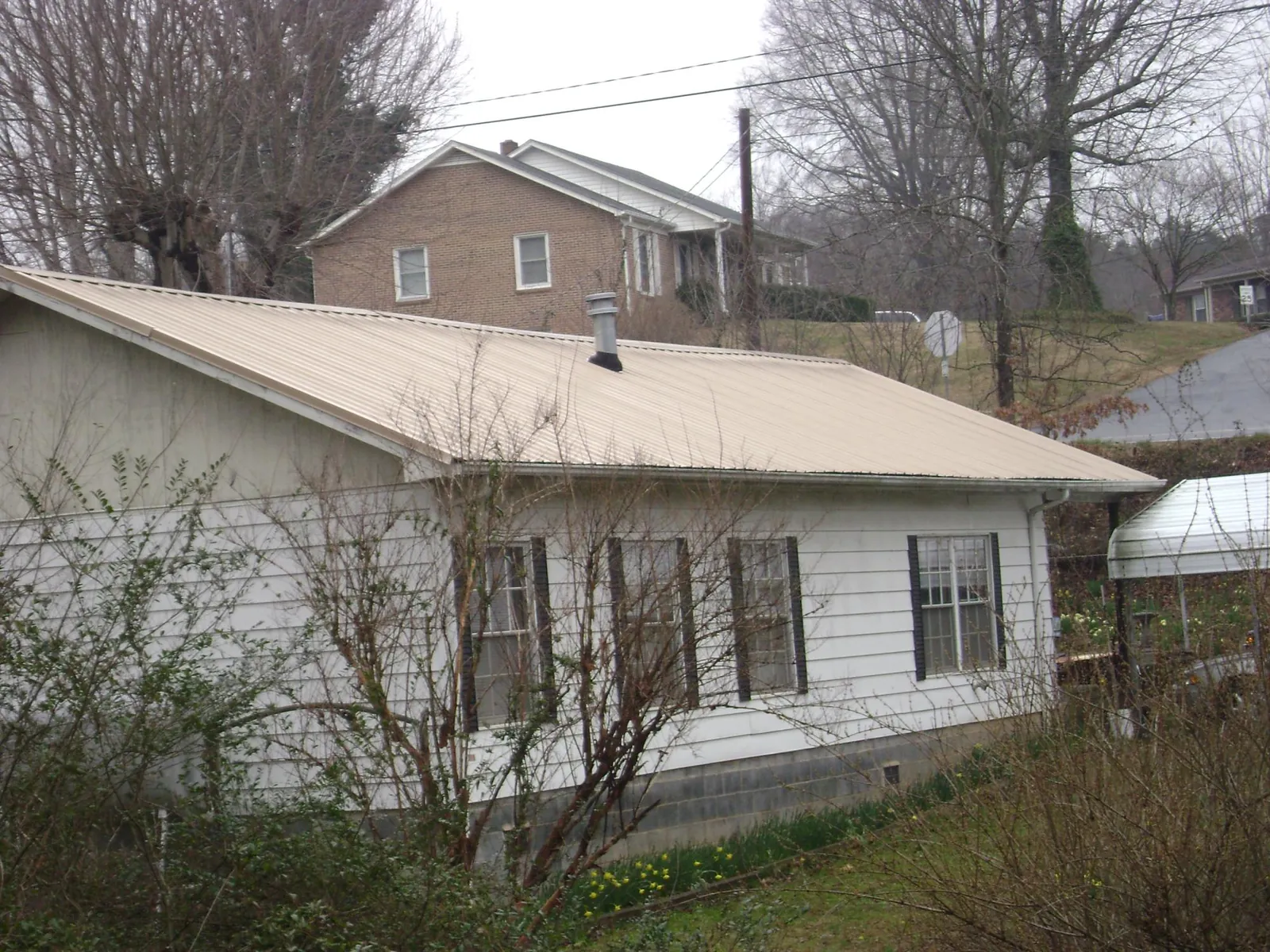 Tan metal roof on a white sided house set into a hillside — Commercial Roofing by Roofing Brothers in Ghent